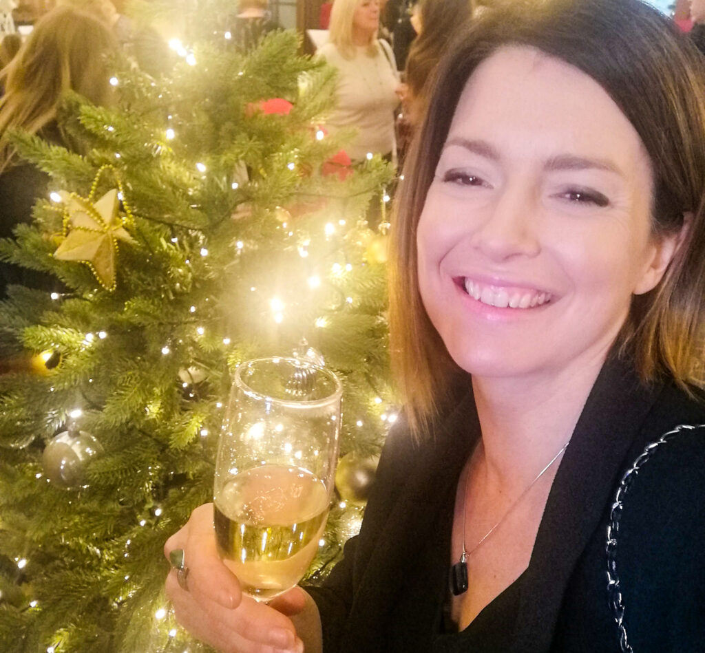 Sian with a glass of champagne in front of a Christmas tree