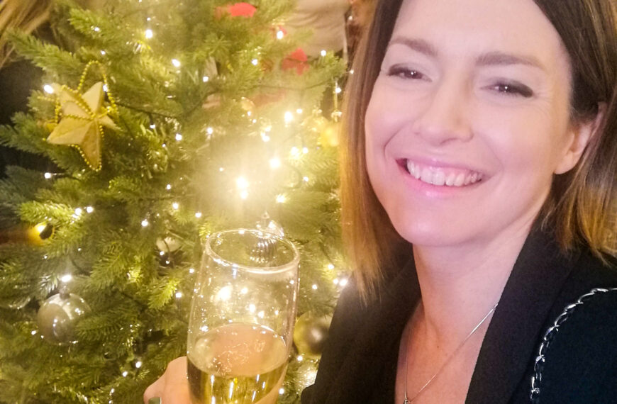 Sian with a glass of champagne in front of a Christmas tree