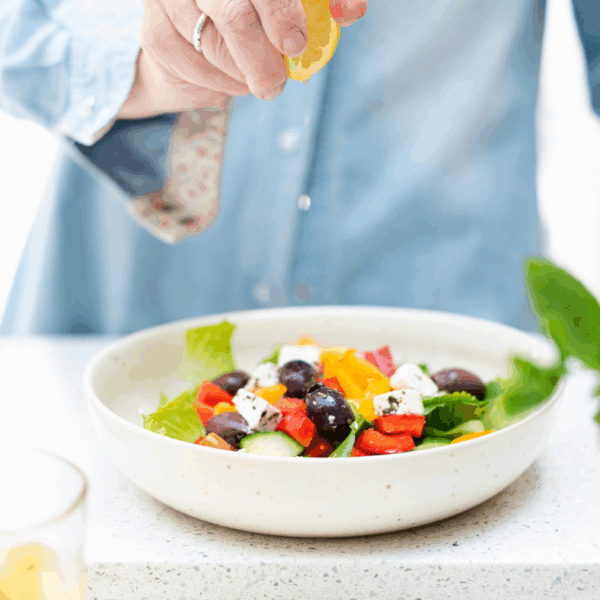 Close-up of a busy professional woman squeezing lemon onto a colourful salad. Soft lighting, calm atmosphere.