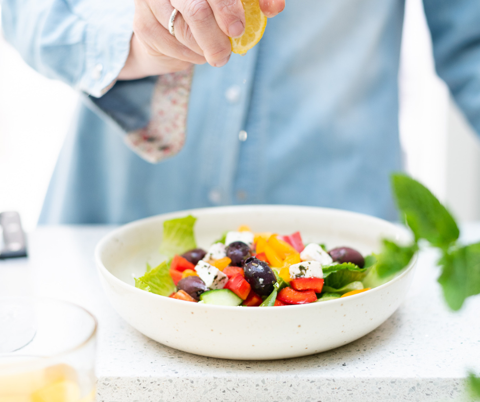 Close-up of a busy professional woman squeezing lemon onto a colourful salad. Soft lighting, calm atmosphere.